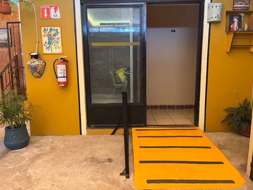 Wheelchair ramp, fire extinguisher, and emergency evacuation signage at the entrance of Mi Casita senior care home in Mexico