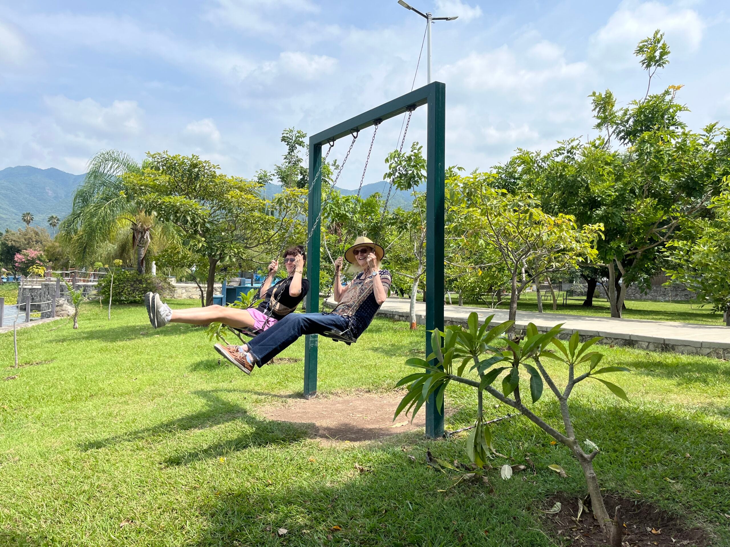 Lake Chapala 1 Adult child and senior mother playing in a swing by a lake in Mexico