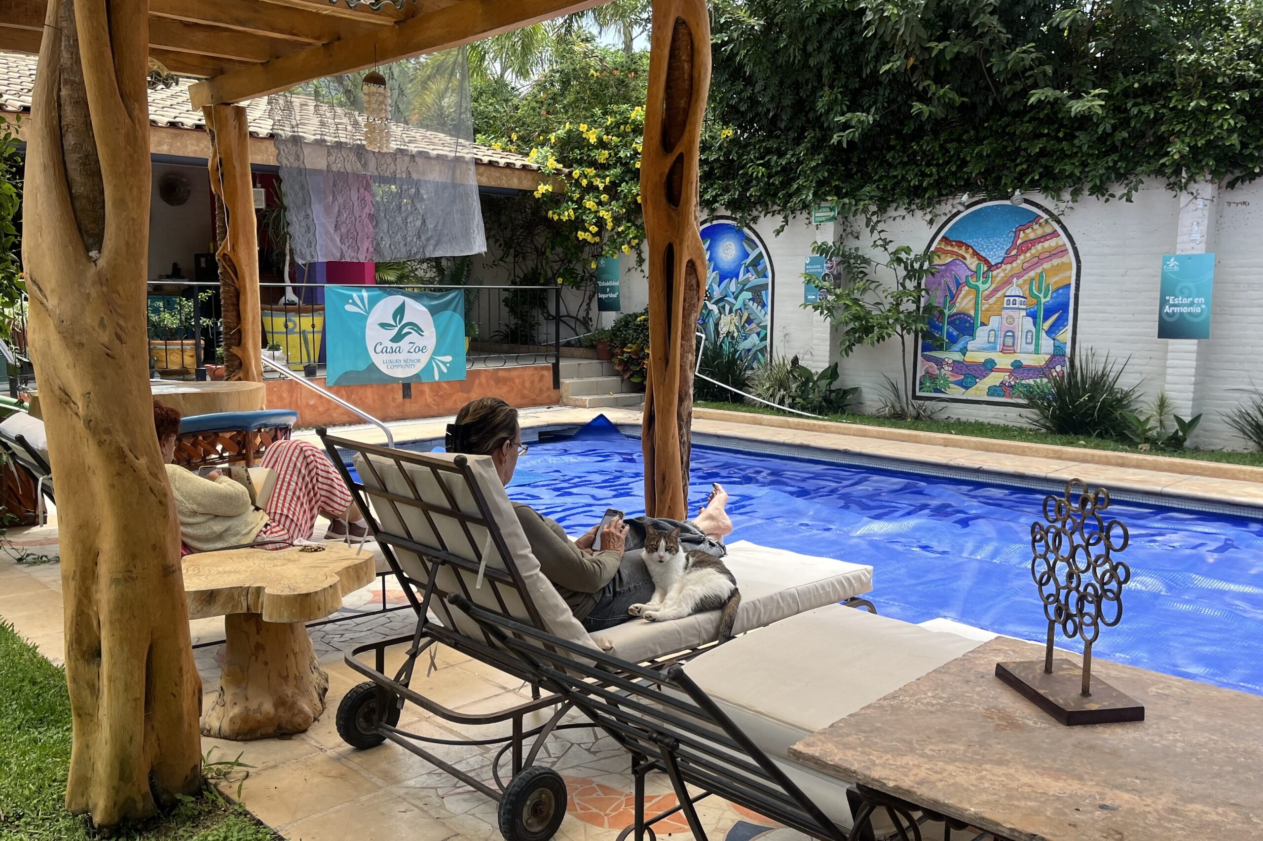 Resident relaxing on a lounge chair with a cat by the pool at Casa Zoe senior community in Ajijic